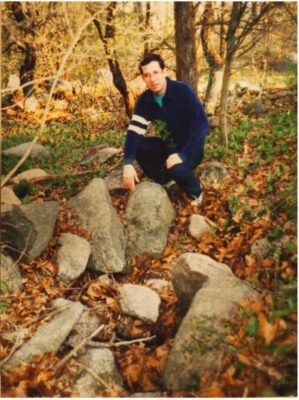 A man squatting among boulders.